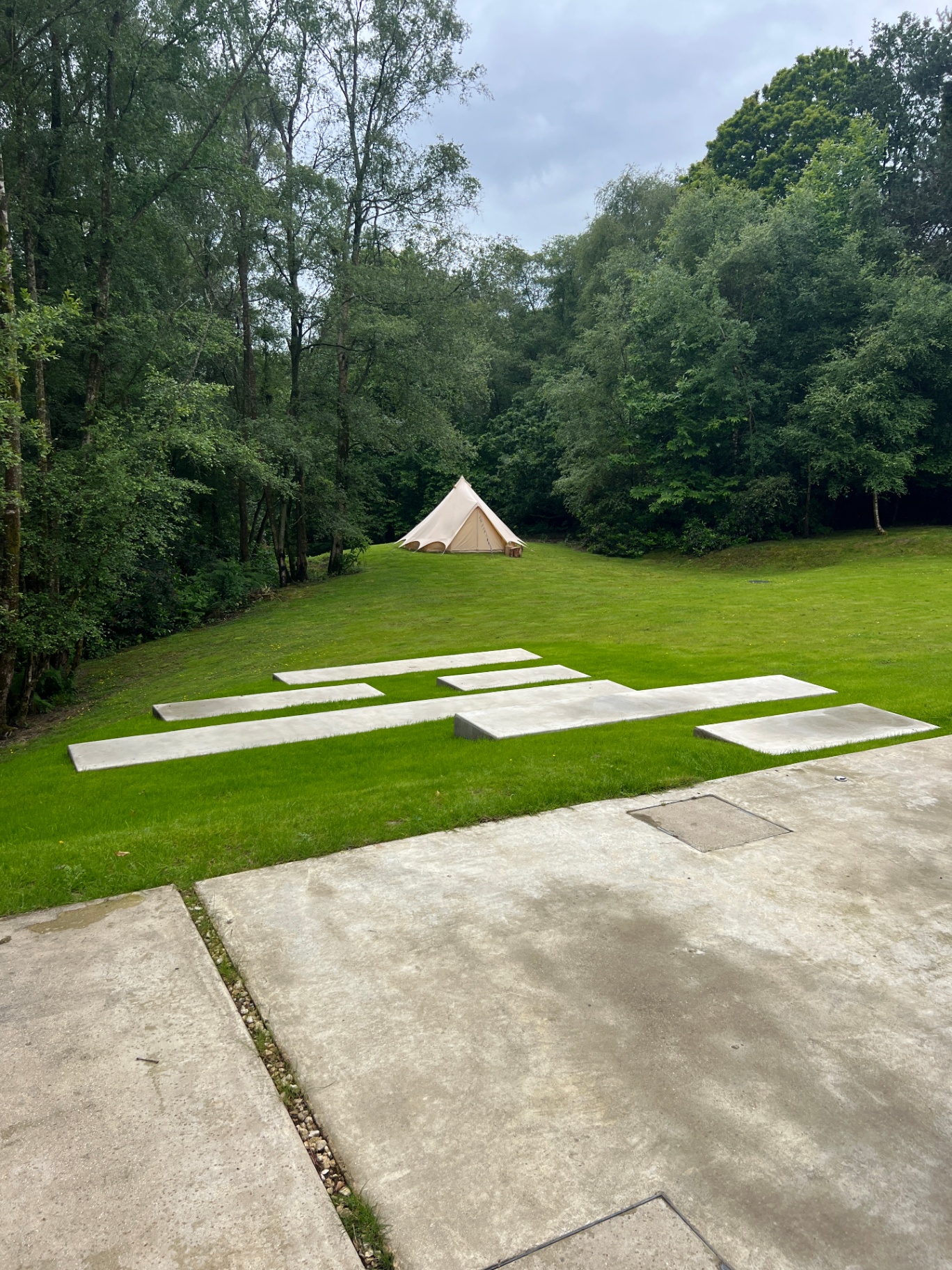 Off-set concrete treads leading across the lawn to a bell tent in the woodland