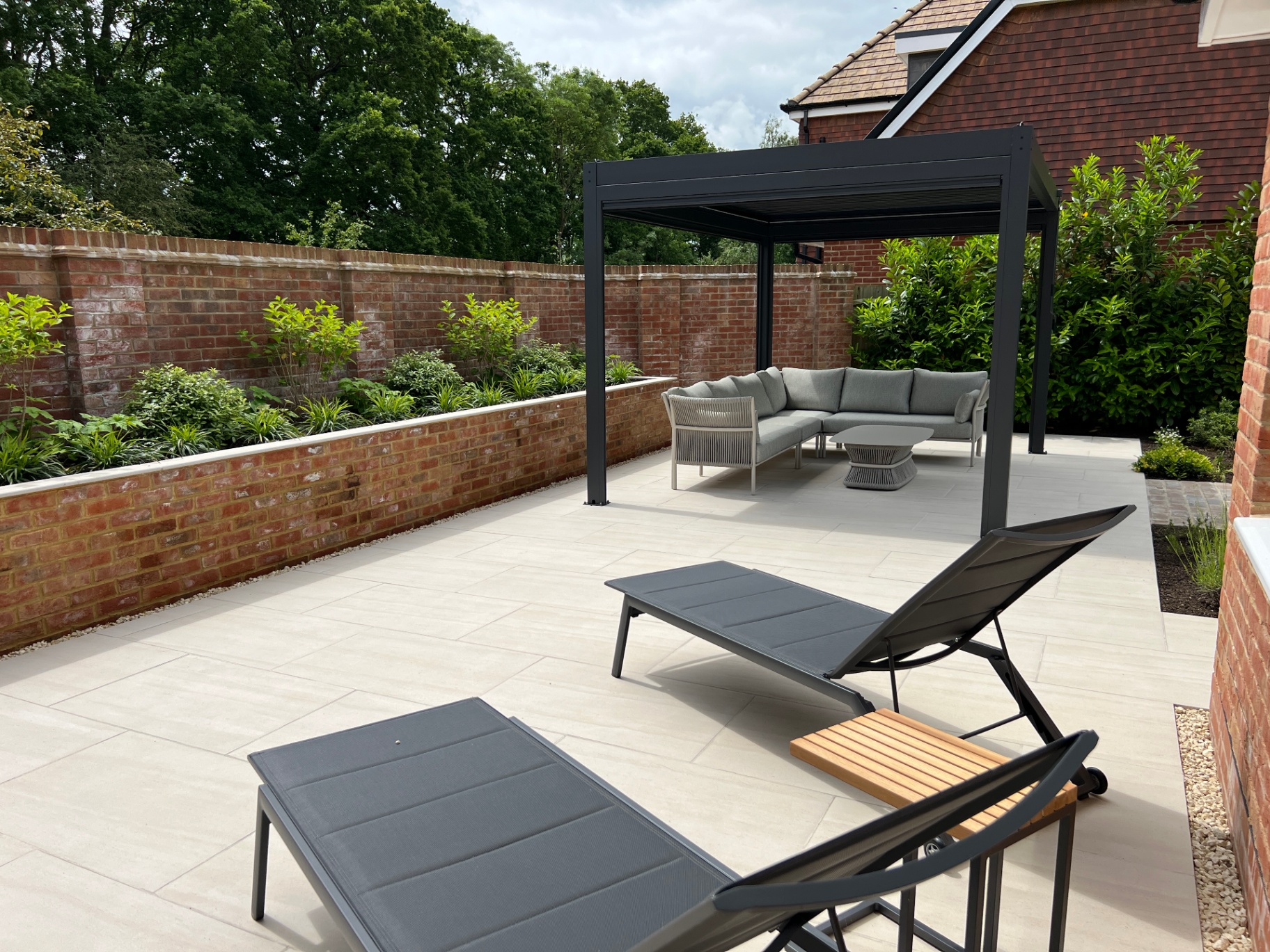 Charcoal aluminium pergola in a walled garden courtyard with loungers and sofa