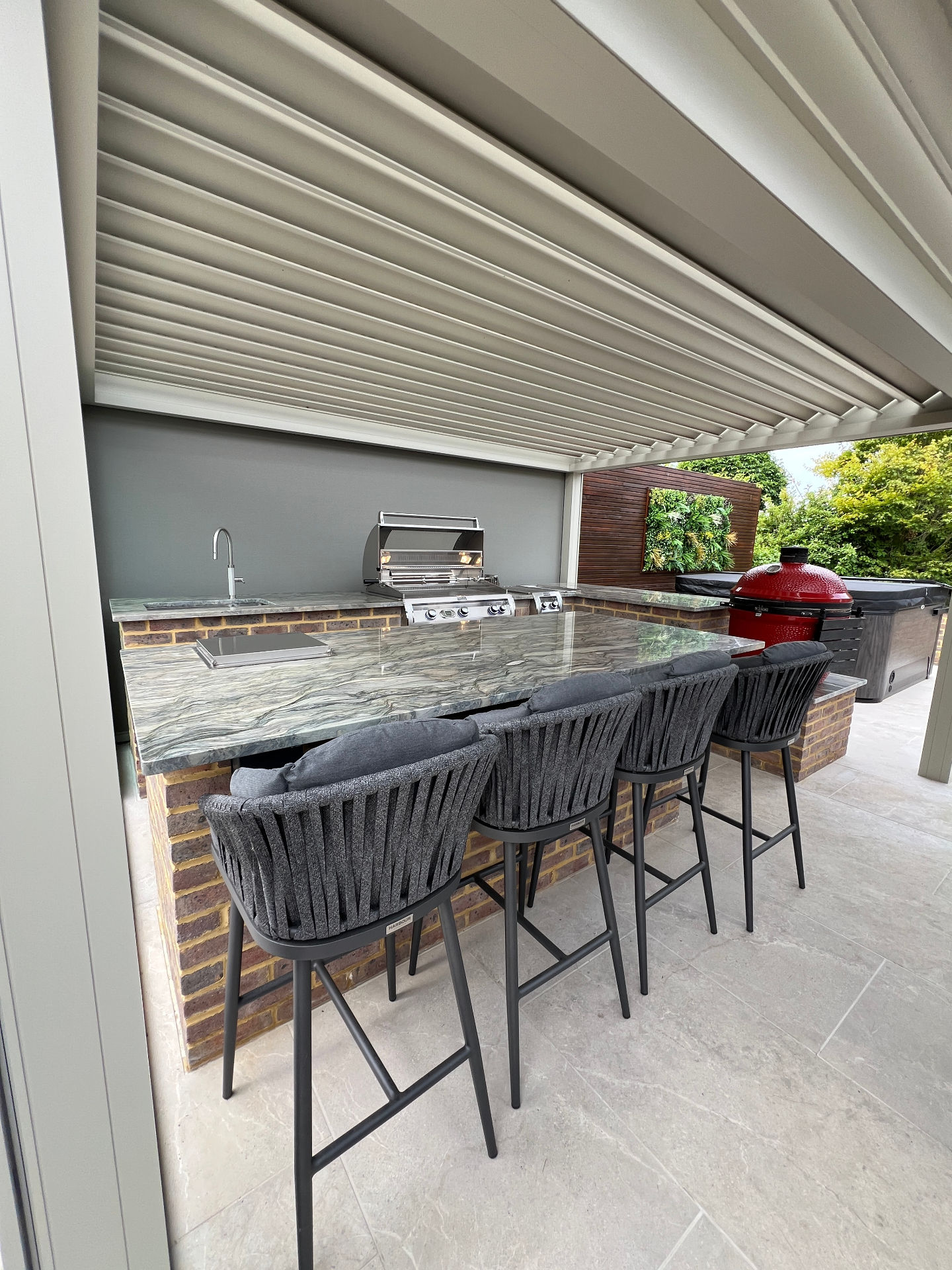 Marble bar with woven barstools beneath louvered pergola