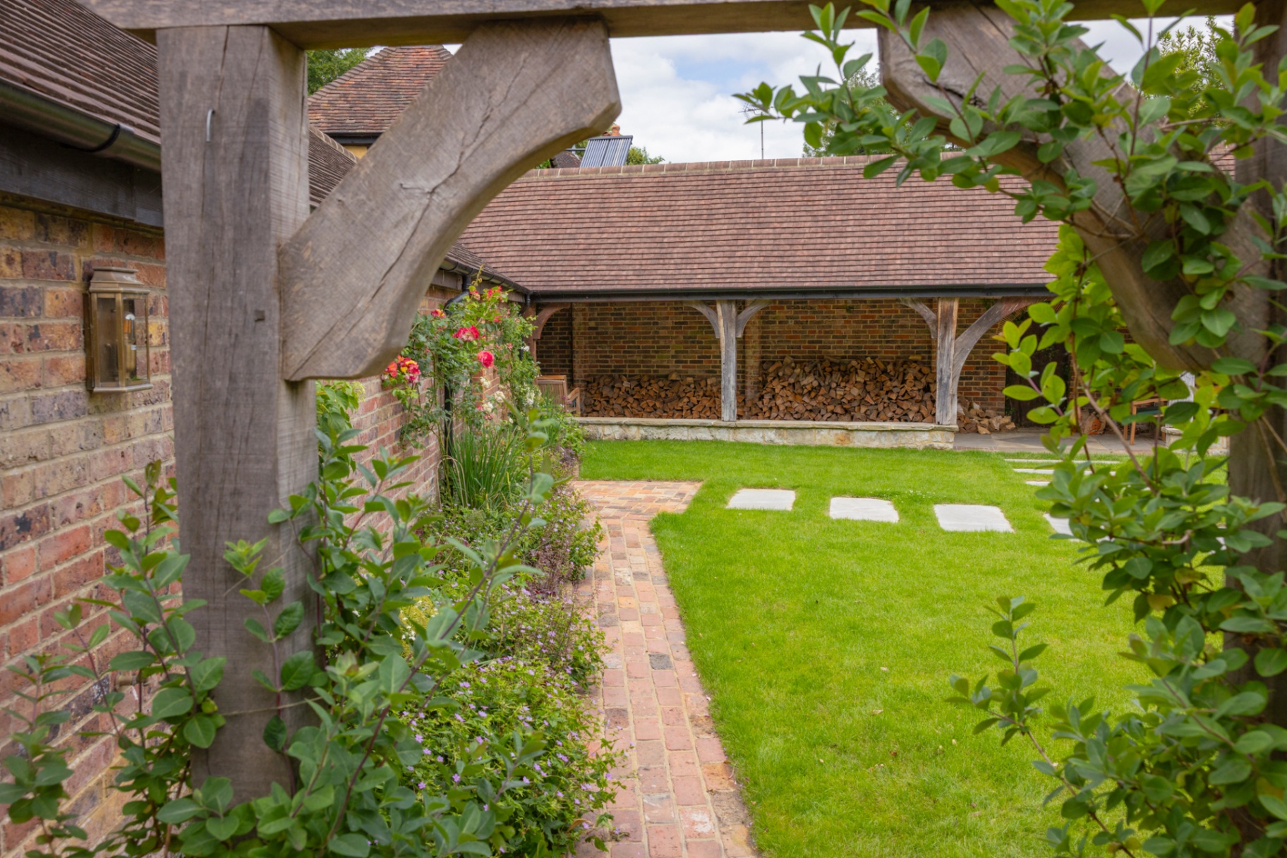 View through oak pergola to brick path and log store