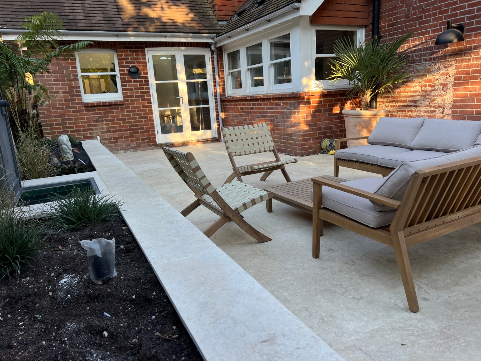 Medi Garden — wider view of the travertine courtyard with woven lounge chairs and planted edges