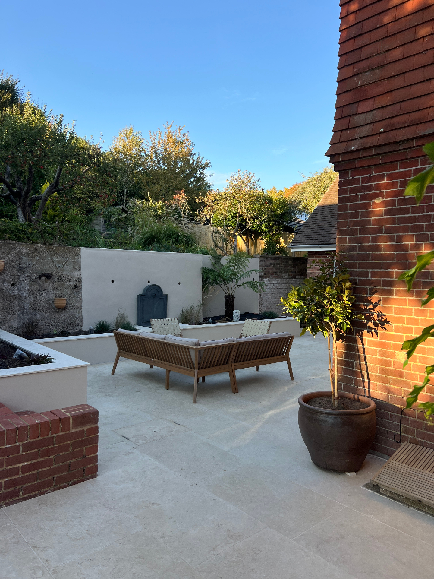 Medi Garden — travertine terrace at golden hour with lead fountain wall and bay tree in terracotta pot