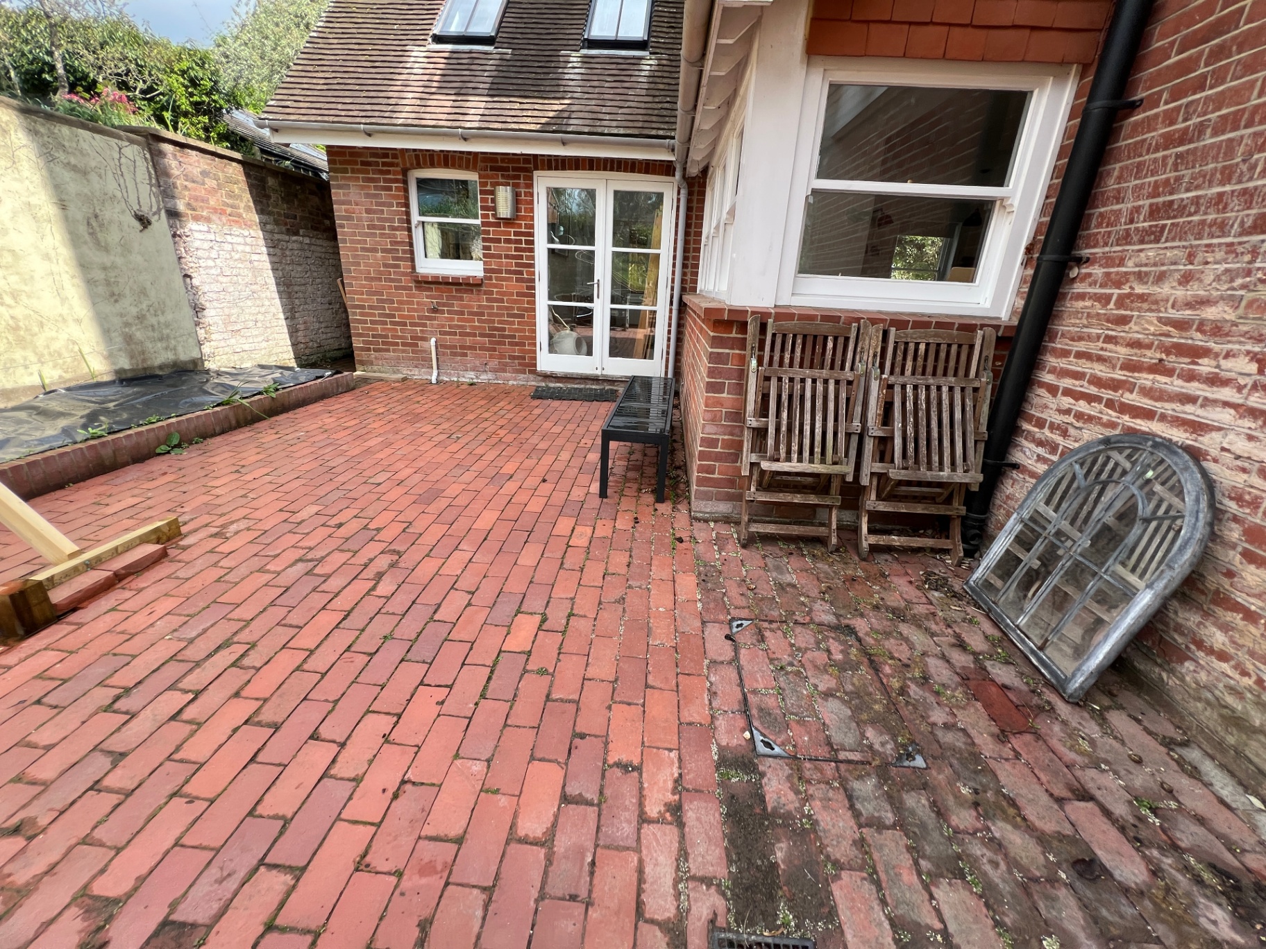 Original courtyard — tired red brick paving with mismatched timber chairs against the house