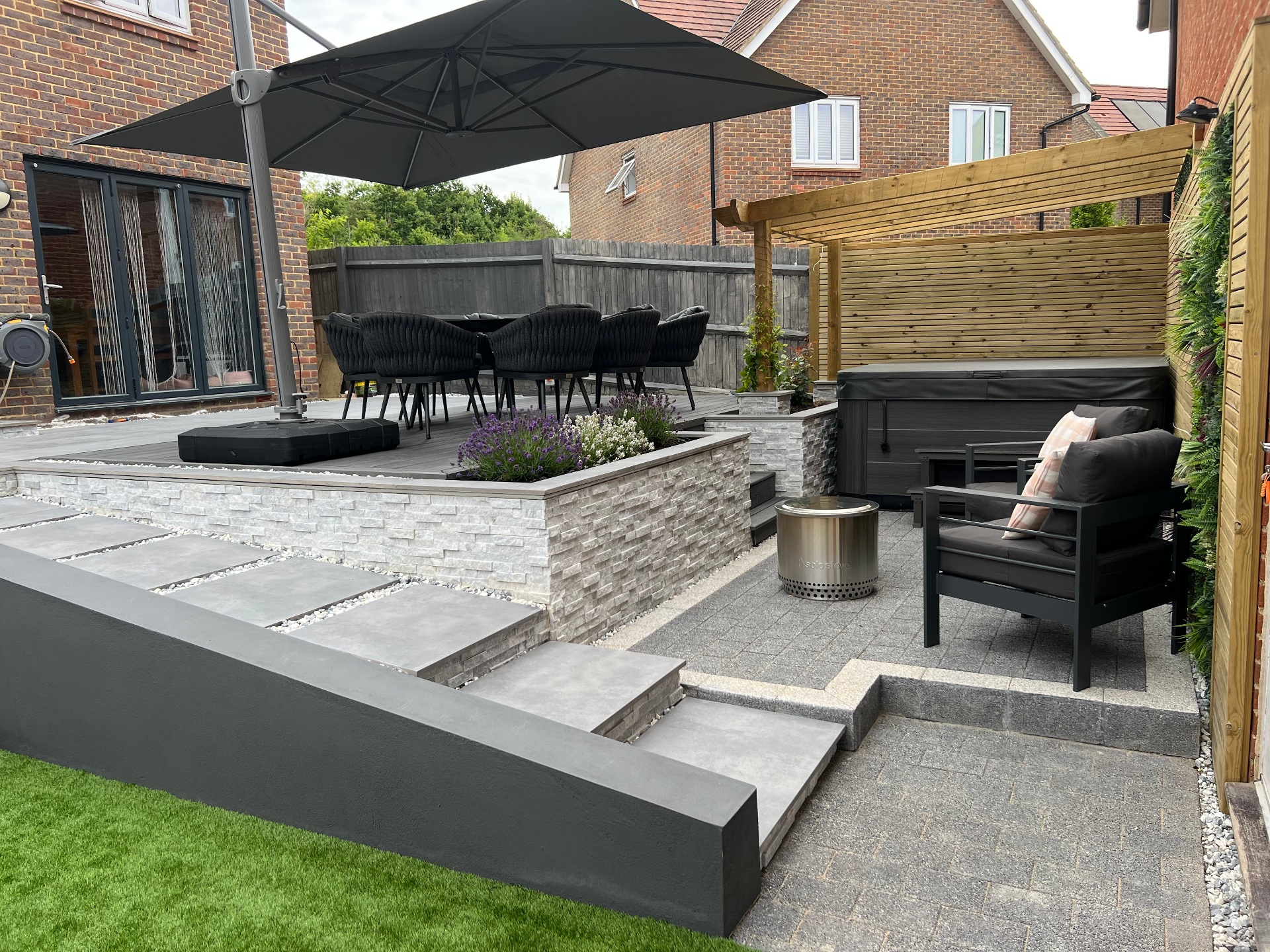 Finished garden — elevated dining terrace, pergola framing and layered stone-clad planters