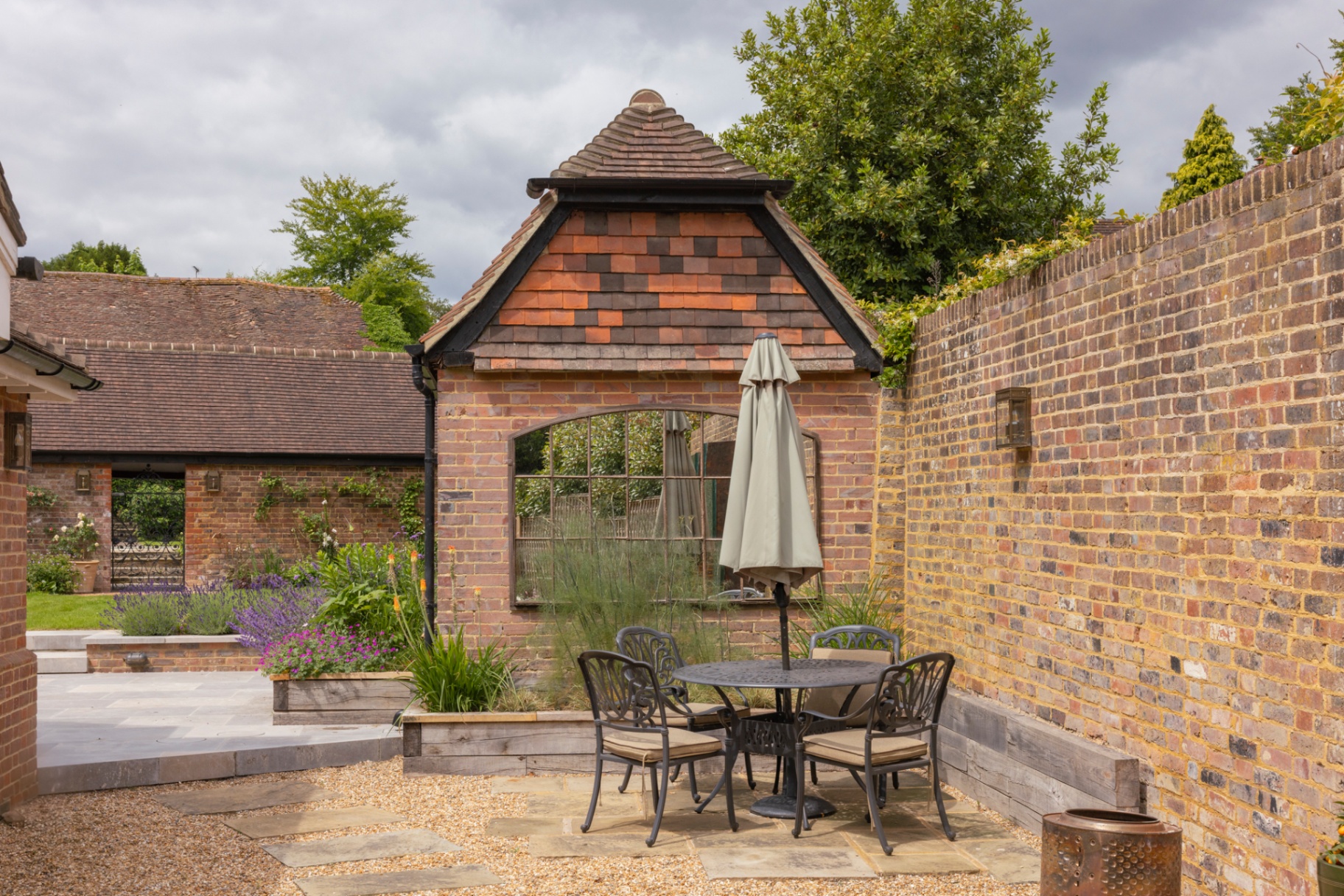 Walled courtyard with reclaimed York stone terrace, lavender beds and tile-hung outbuilding with arched window