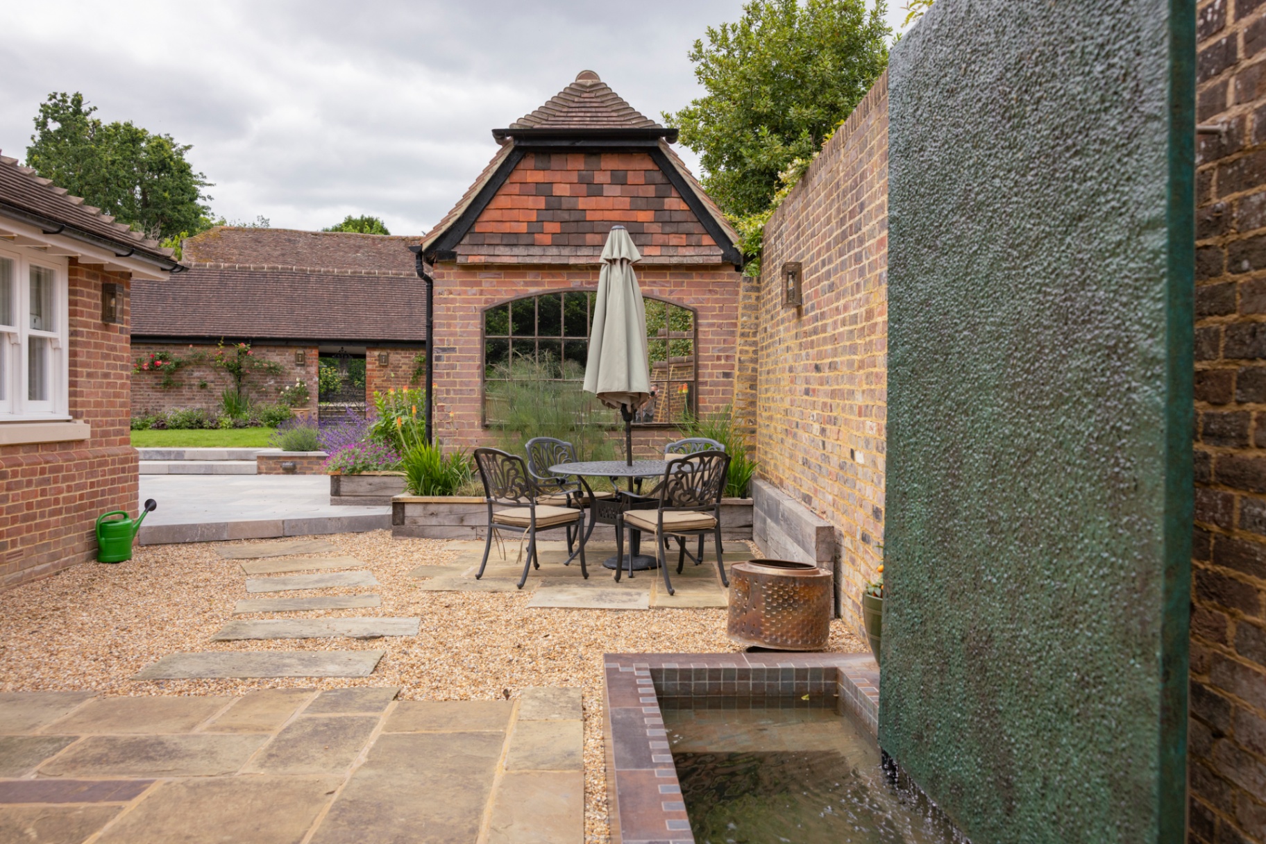 Stepping stones across the gravel courtyard leading to the cast iron dining set with the lava wall in the foreground