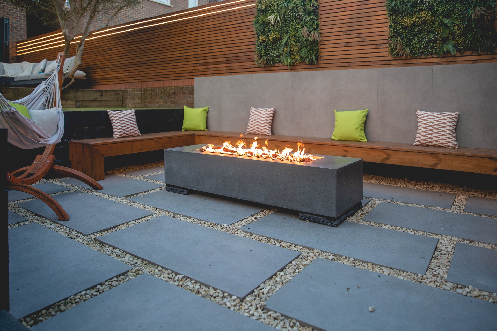 Fire pit glowing on porcelain paving with gravel joints and wraparound bench seating