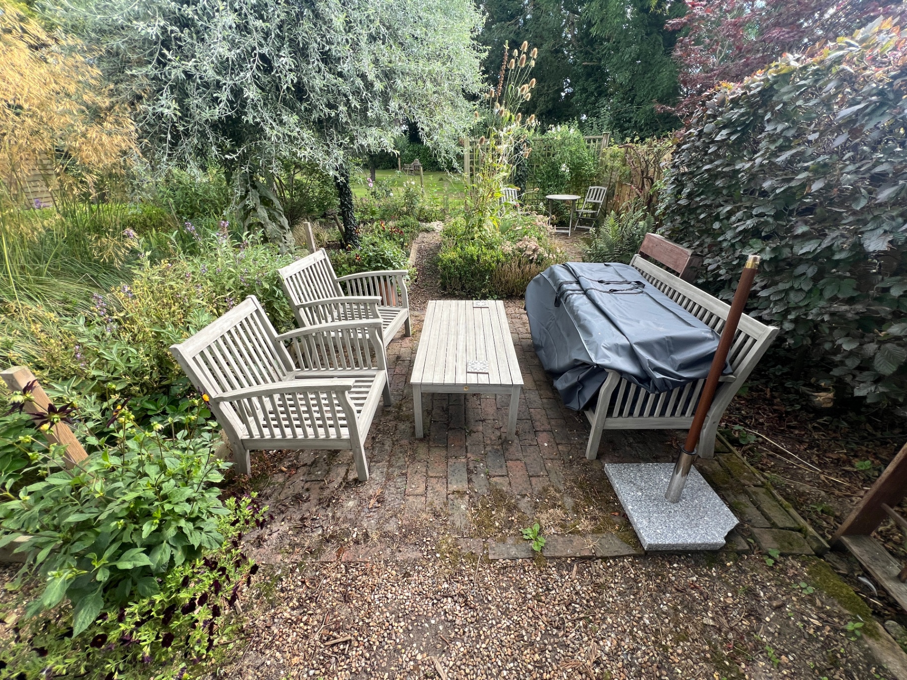 Original garden — weathered teak seating on a small brick patio surrounded by overgrown borders